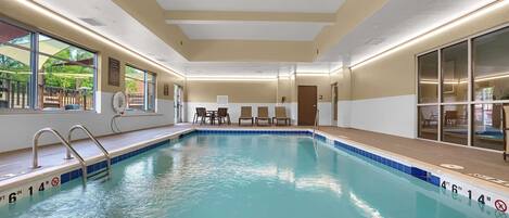 An indoor swimming pool with clear water, a lifeguard chair, and a sunshade by the window.