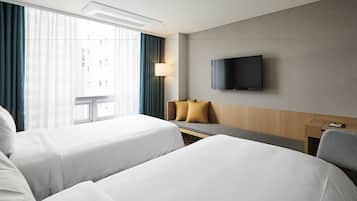 Habitación de hotel con dos camas, un escritorio, un televisor y una ventana con cortinas.