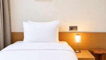 Habitación de hotel con cama, mesita de noche con lámpara y enchufe en la pared.
