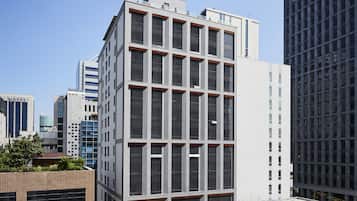 Un edificio moderno con una fachada de ventanas en forma de cuadrícula, una terraza en la azotea y un área de entrada ajardinada.