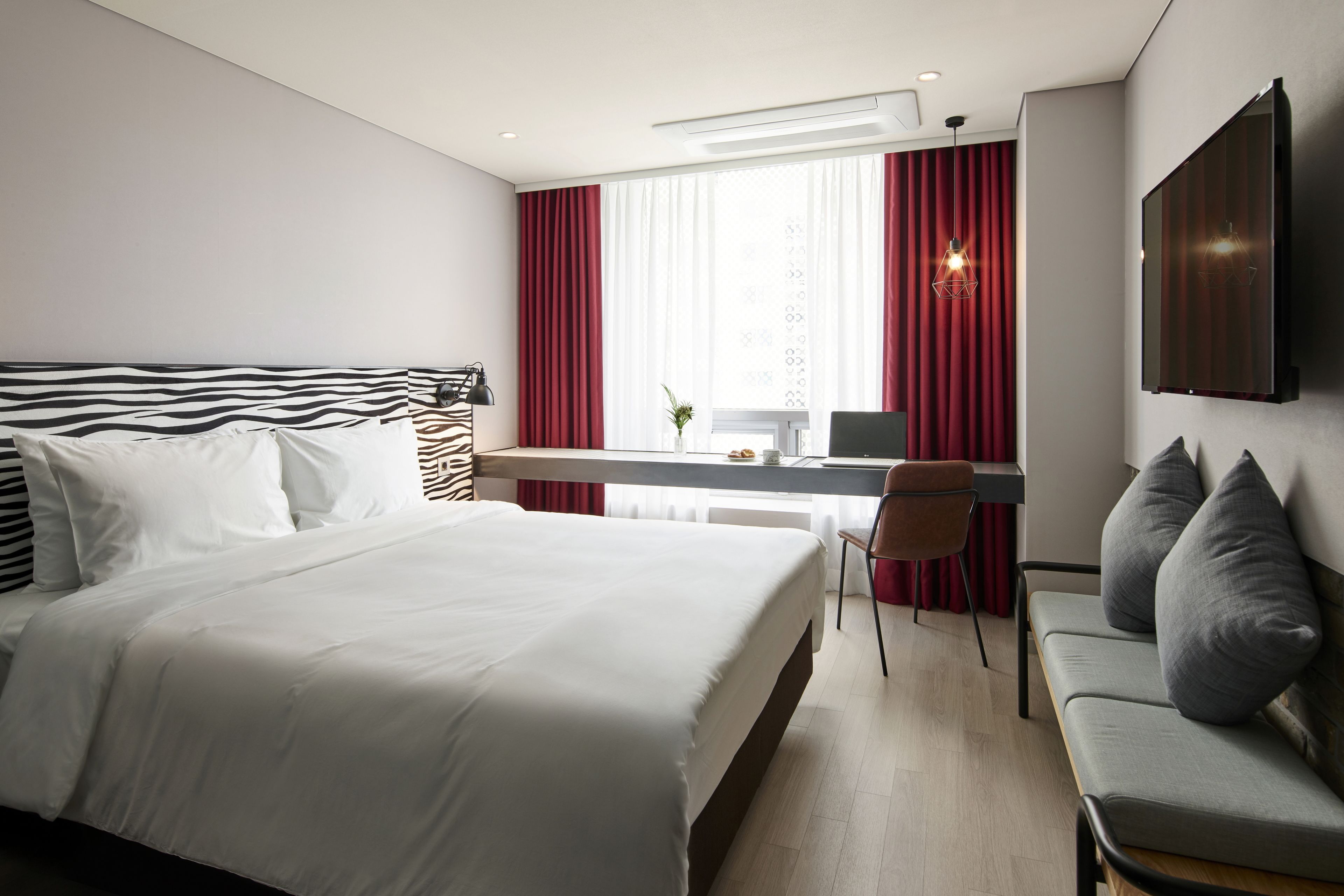 A modern hotel room with a large bed, a desk, a chair, and a TV mounted on the wall.