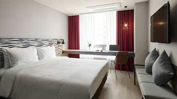 A modern hotel room with a large bed, a desk, a chair, and a TV mounted on the wall.