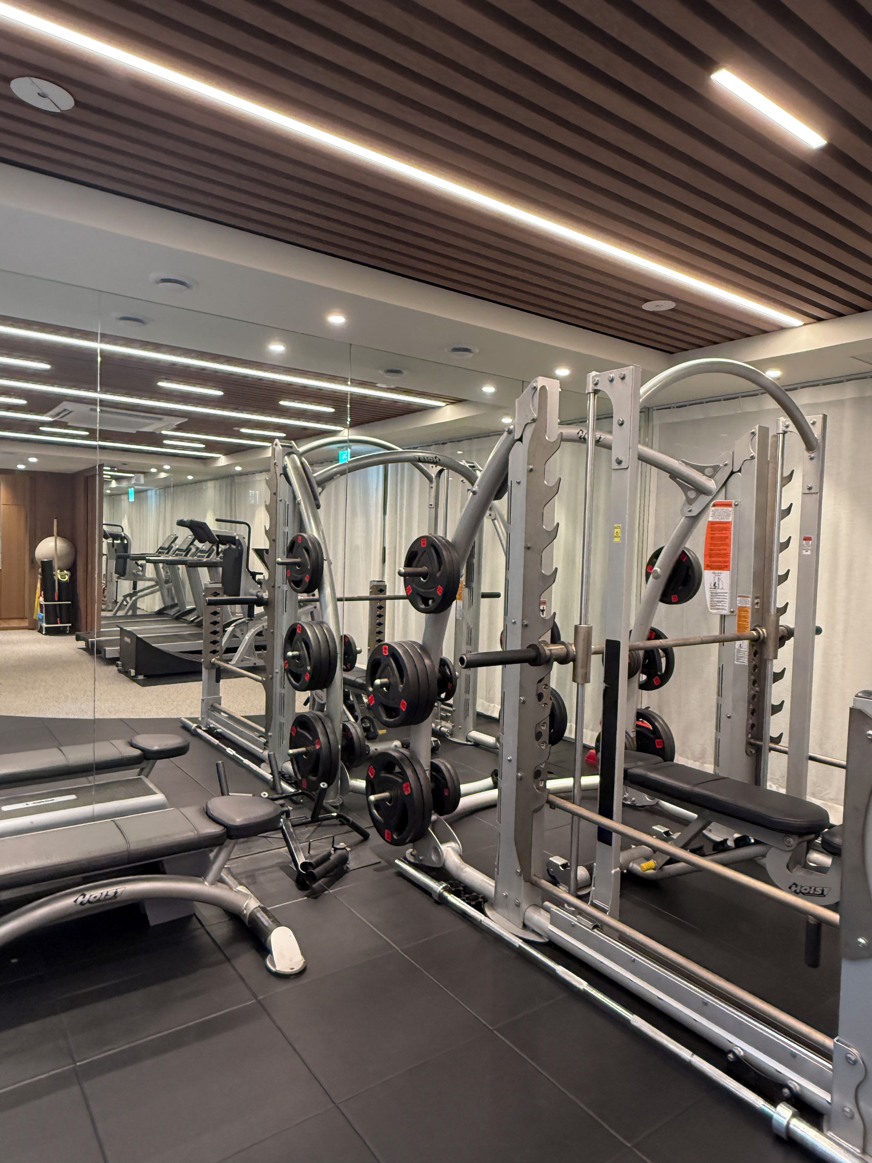 Uma academia com equipamentos de musculação, esteiras e um painel de espelhos.