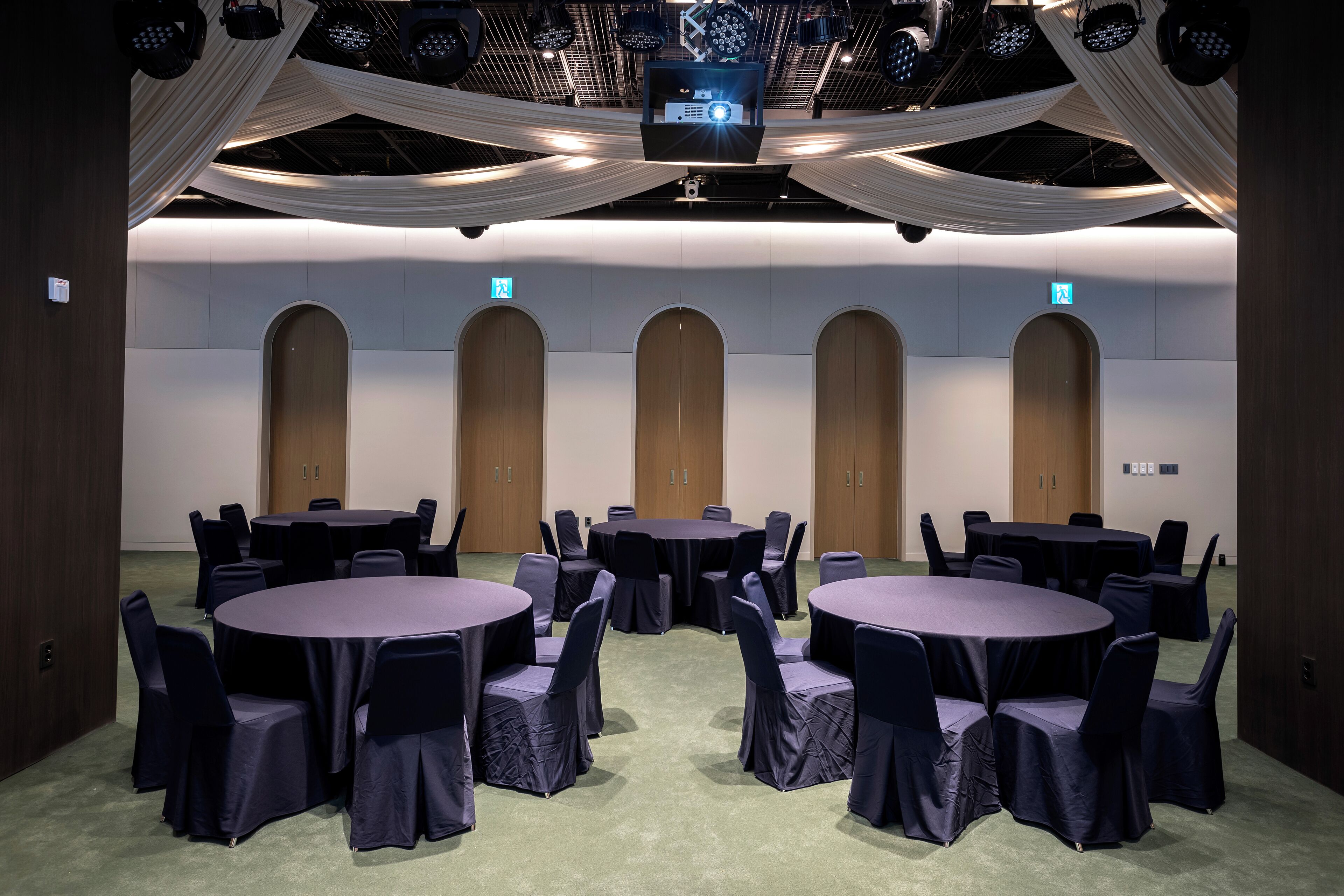 A conference room with multiple tables and chairs, a large screen, and a ceiling with draped fabric.