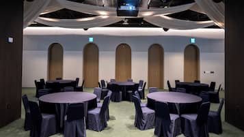 A conference room with multiple tables and chairs, a large screen, and a ceiling with draped fabric.