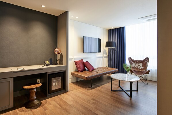 A modern hotel room with a wooden floor, a sofa, a small round table, a TV mounted on the wall, and a window with curtains. - Hotel Newv (Seoul)