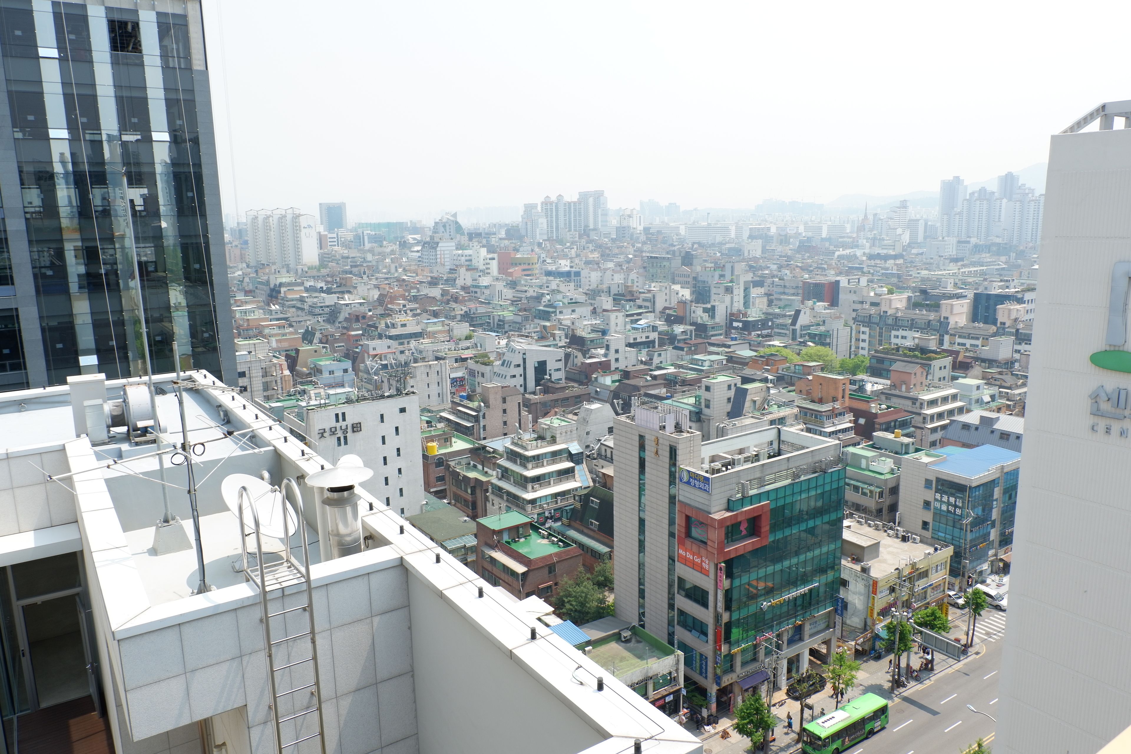 Un paisaje urbano con varios edificios, incluyendo una construcción moderna de vidrio y una estructura tradicional con techo verde.