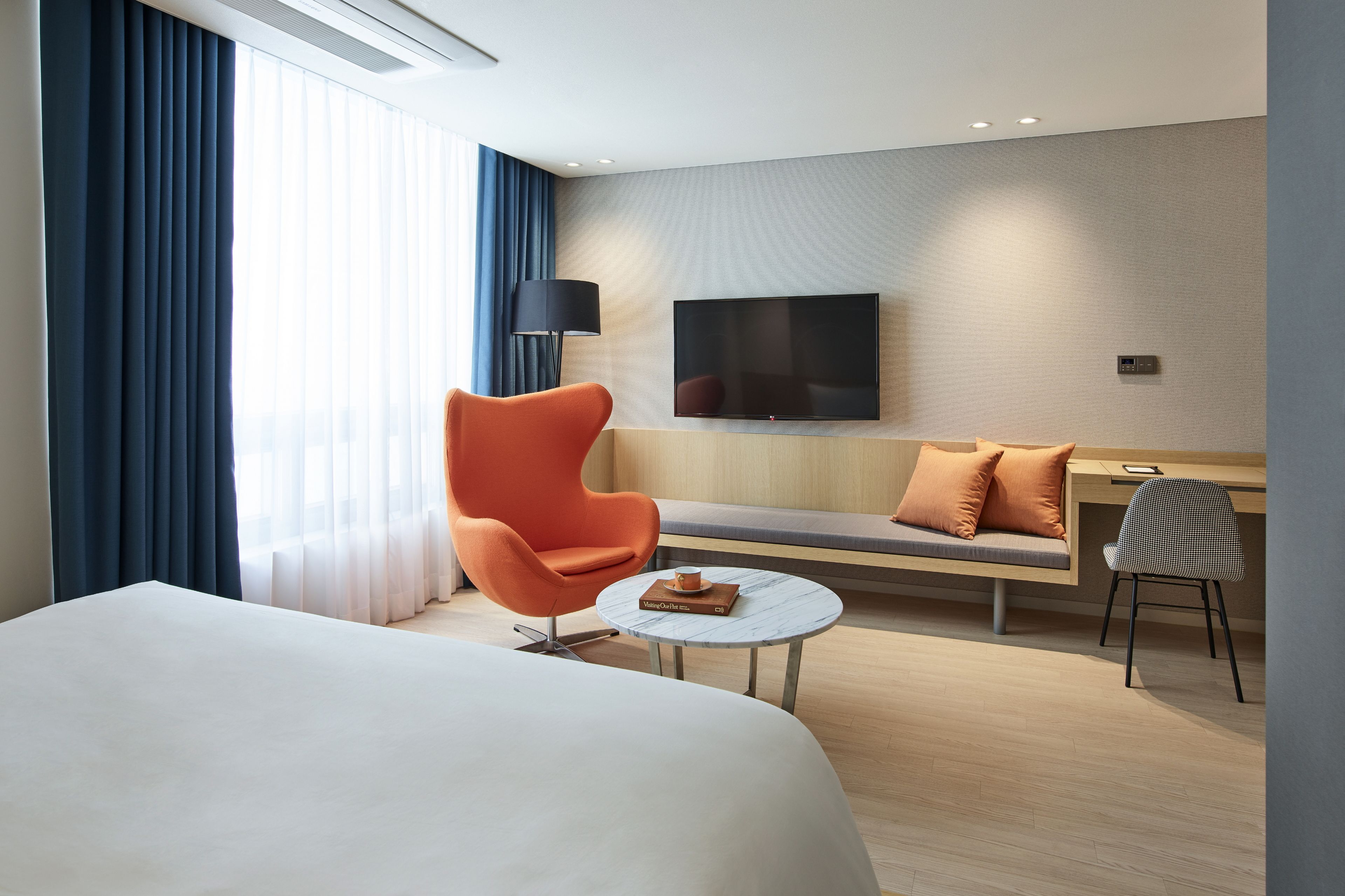 A modern hotel room with a large bed, a sofa, a round coffee table, and a TV mounted on the wall.