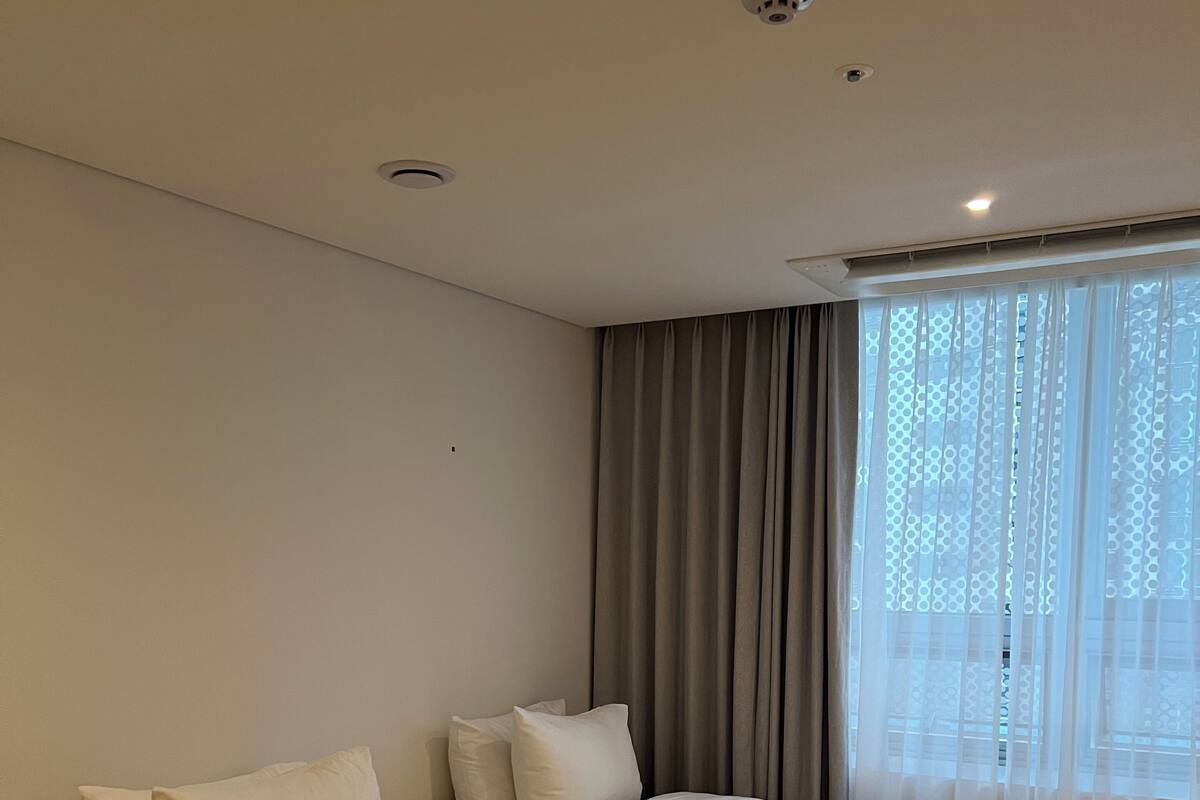Una habitación de hotel con dos camas, un ventanal con cortinas e iluminación empotrada en el techo.