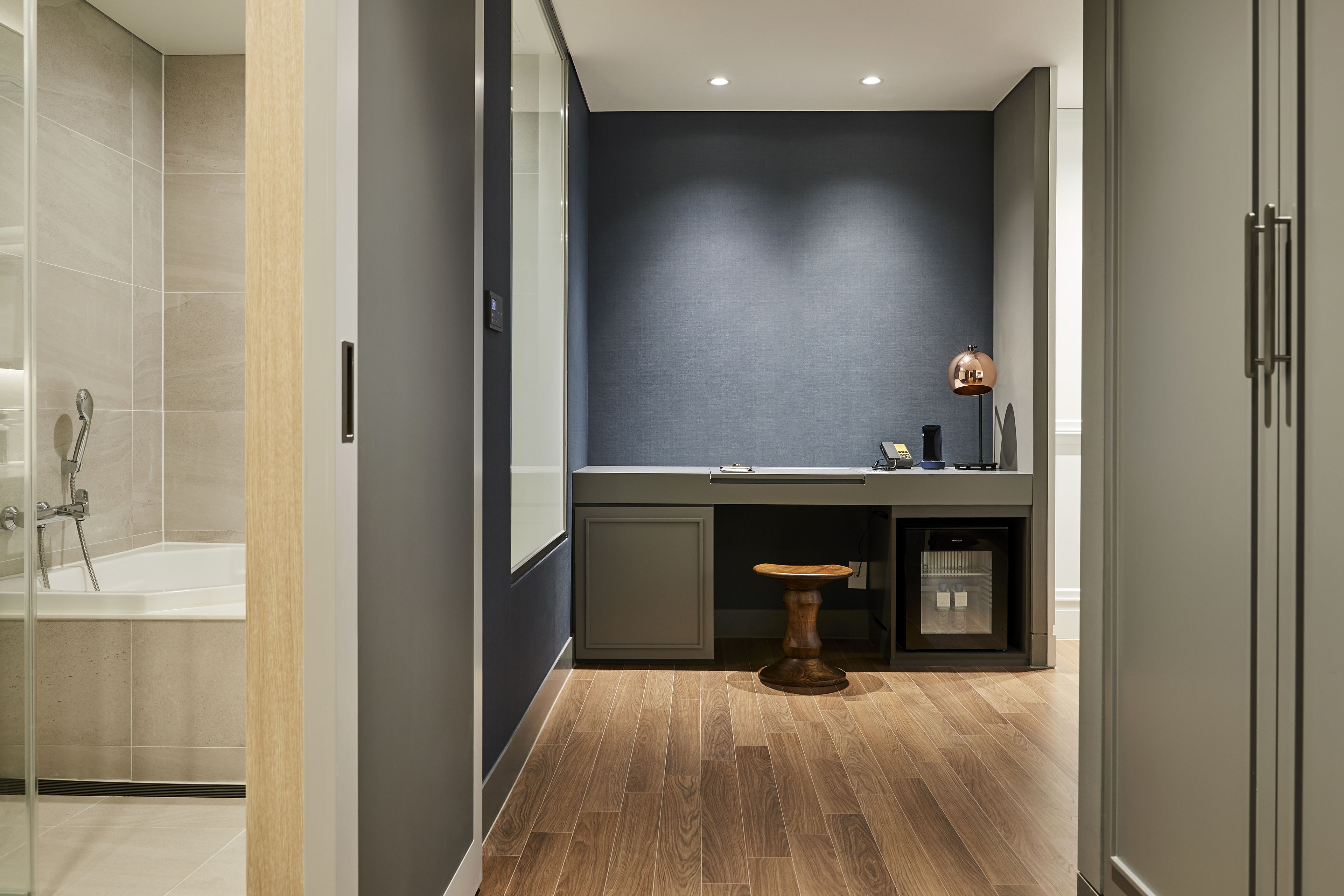 A modern bathroom with a bathtub, a vanity with a mirror, and a small stool.