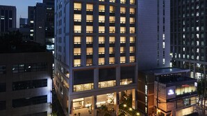A modern hotel with multiple floors, large windows, and a well-lit entrance area with outdoor seating. - Hotel Newv (Seoul)