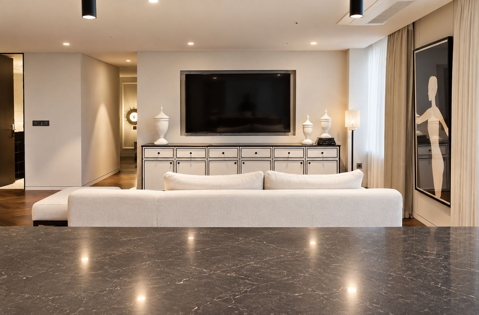 A modern living room with a large flat-screen TV, a white sofa, and a marble floor.