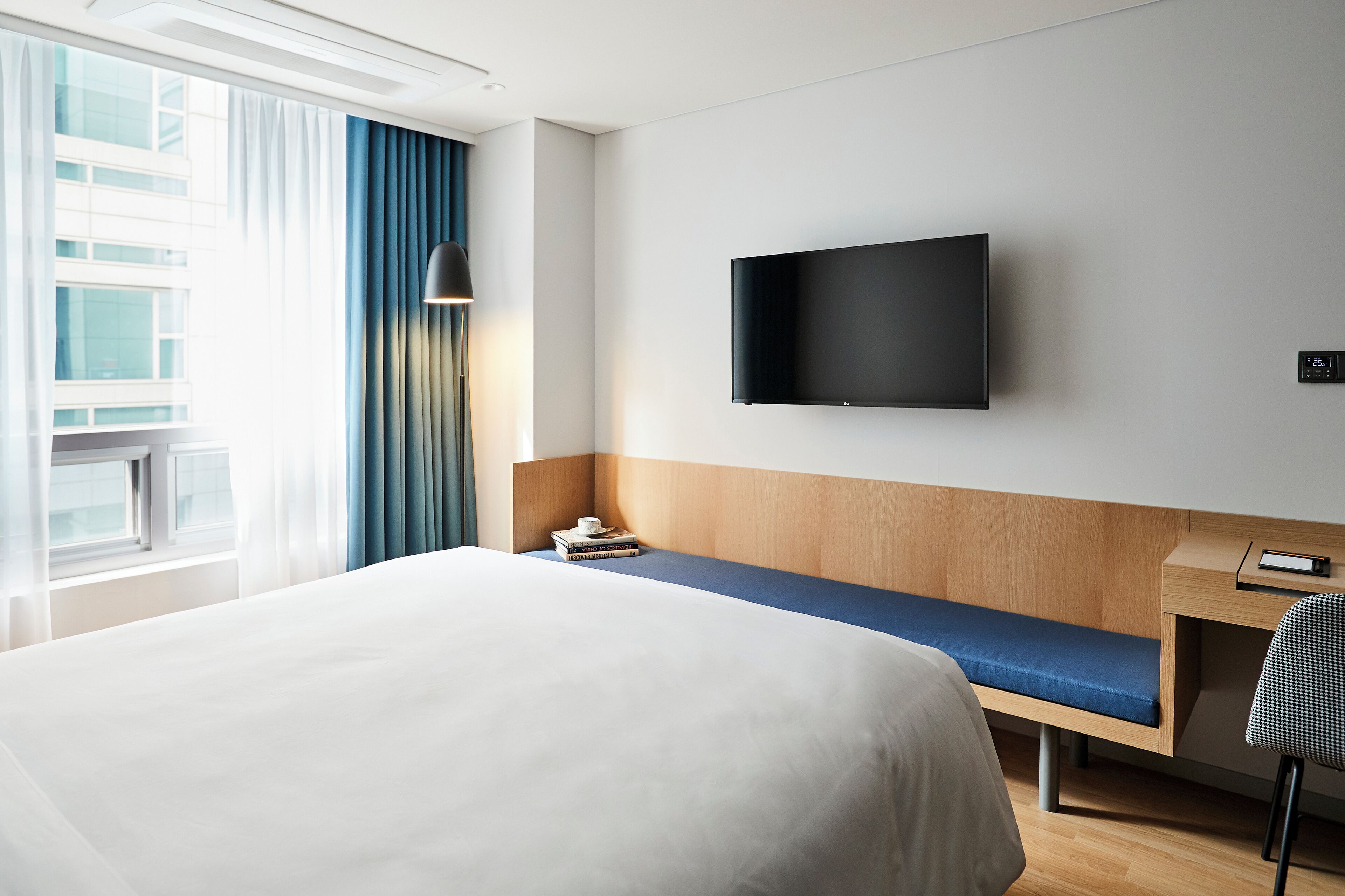 Habitación de hotel con una cama grande, un escritorio con silla, un televisor de pantalla plana en la pared y una ventana con cortinas.