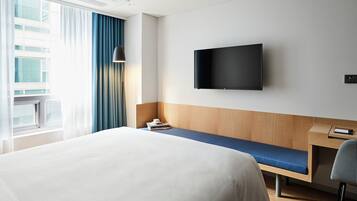Habitación de hotel con una cama grande, un escritorio con silla, un televisor de pantalla plana en la pared y una ventana con cortinas.