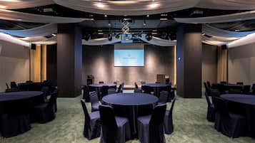 A conference room with round tables and chairs, a projector screen, and draped fabric on the ceiling.
