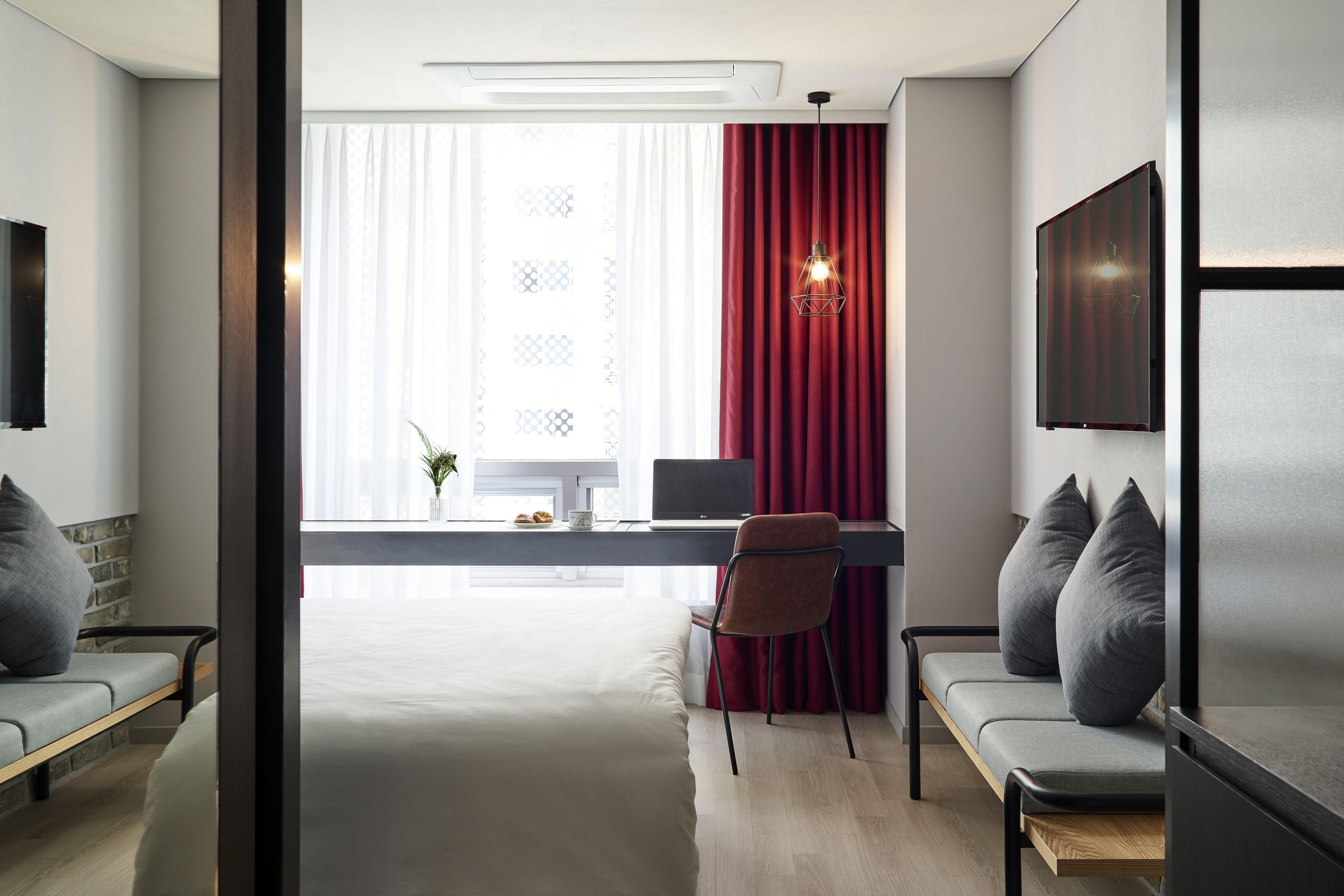 Una habitación de hotel moderna con escritorio, dos sillas, una cama y un ventanal con cortinas.