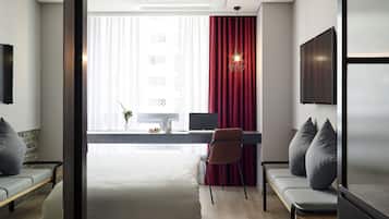 Una habitación de hotel moderna con escritorio, dos sillas, una cama y un ventanal con cortinas.