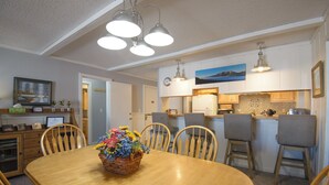 A dining area with a wooden table, chairs, and a centerpiece of flowers. There are three pendant lights above the table. - Ski-In/Out! 3/2 Slopeside Spacious Condo w/ Amazing Mtn Views!! (Mt. Crested Butte)