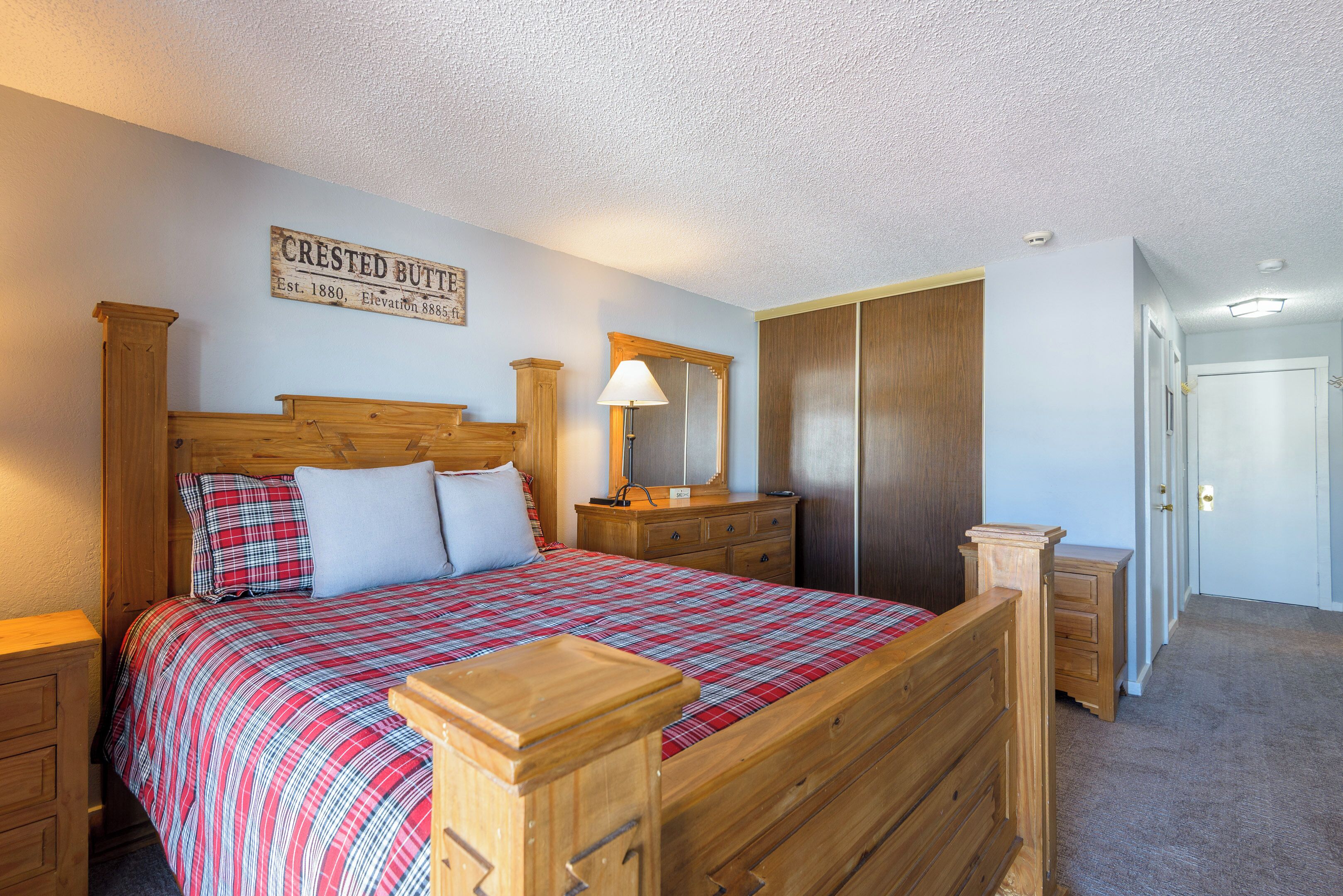 A bedroom with a wooden bed, a nightstand, a dresser, a mirror, and a door.