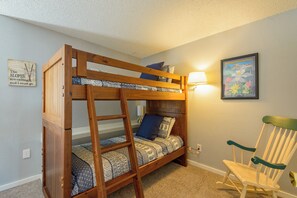 A bunk bed with a ladder, a chair, and a wall-mounted lamp.