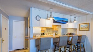 A compact kitchen with a central island, bar stools, a clock, and a painting on the wall. - Ski-In/Out! 3/2 Slopeside Spacious Condo w/ Amazing Mtn Views!! (Mt. Crested Butte)