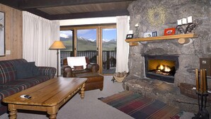 A cozy living room with a stone fireplace, a sofa, a coffee table, and a view of mountains through large windows. - Location is Everything! Ski-In/Out Condo, No Stairs, End Unit + VIEWS (Mt. Crested Butte)