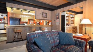 A cozy living room with a plaid sofa, a kitchen area with wooden cabinets, and a bookshelf. - Location is Everything! Ski-In/Out Condo, No Stairs, End Unit + VIEWS (Mt. Crested Butte)