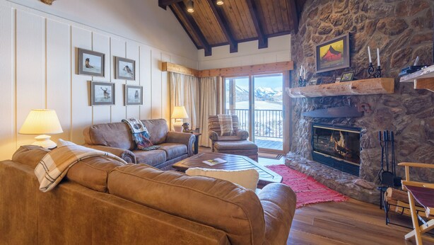 Una sala de estar acogedora con sofás de cuero, una chimenea, cuadros en la pared y vistas a la montaña a través de grandes ventanales.