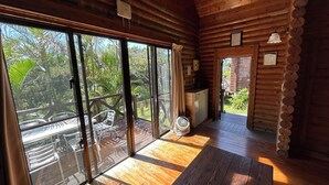 A wooden cabin with large sliding glass doors leading to an outdoor deck. Inside, there is a wooden floor, a small table, and a fan. - Tokashiki Guest House (Tokashiki)