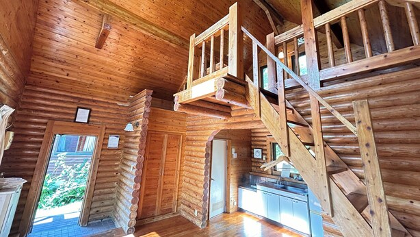 A log cabin interior with a wooden staircase, a kitchen area, and a door leading outside. - Tokashiki Guest House (Tokashiki)