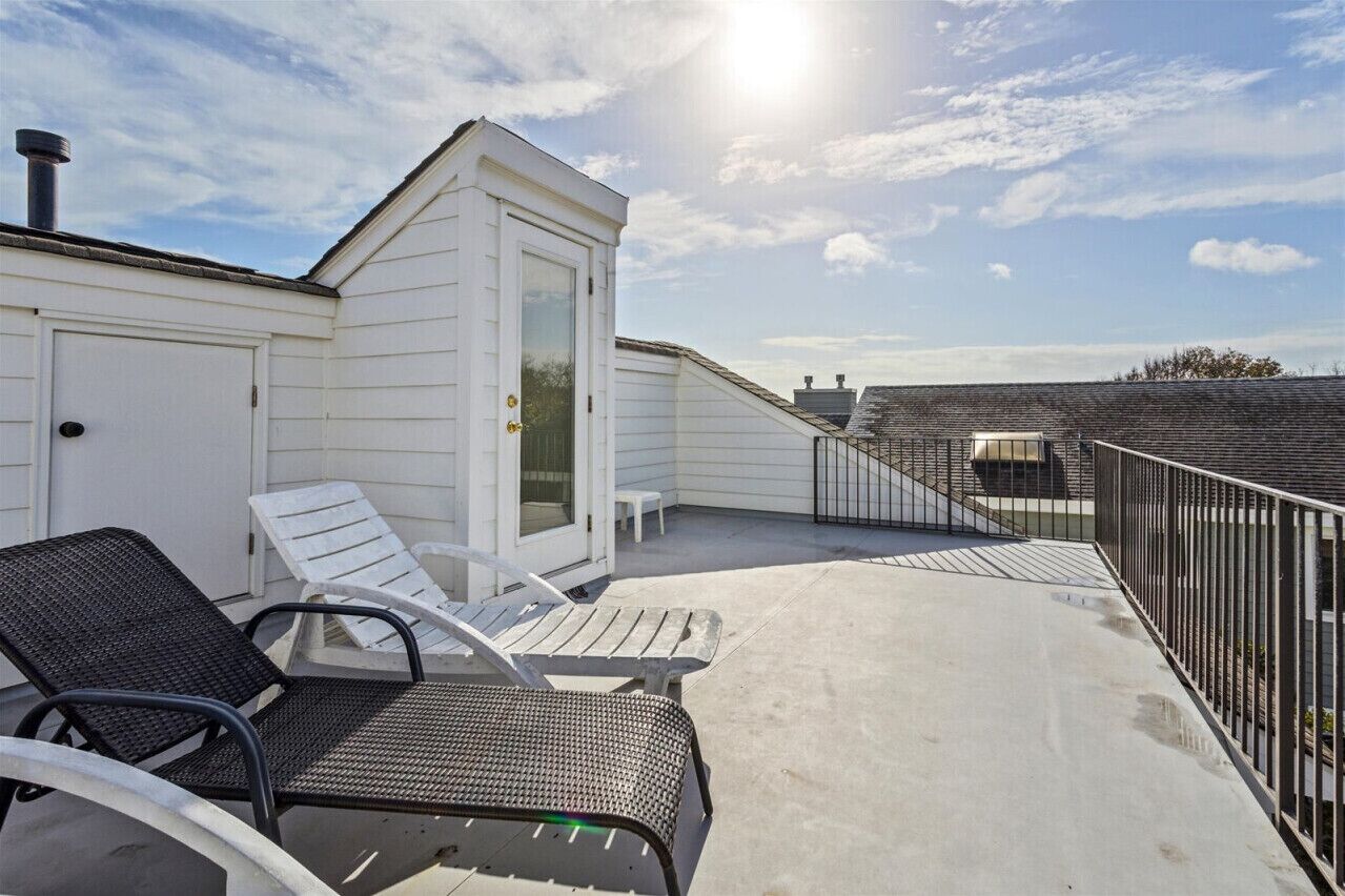 A rooftop terrace with two lounge chairs, a small table, and a white building with a door.