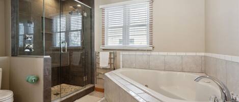 A bathroom with a glass-enclosed shower, a large bathtub, and a window with blinds.