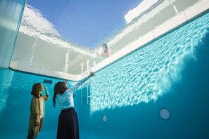 Uma piscina interior com água cristalina, uma escada e uma pessoa a nadar.