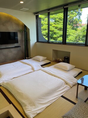Een hotelkamer met een bed, een televisie en een raam met uitzicht op groen.