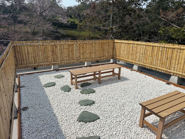 A wooden bench and table set on a gravel surface, surrounded by a bamboo fence.