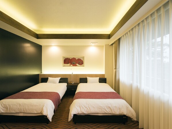 Une chambre d’hôtel avec deux lits, un tableau au mur et une grande fenêtre avec des rideaux.