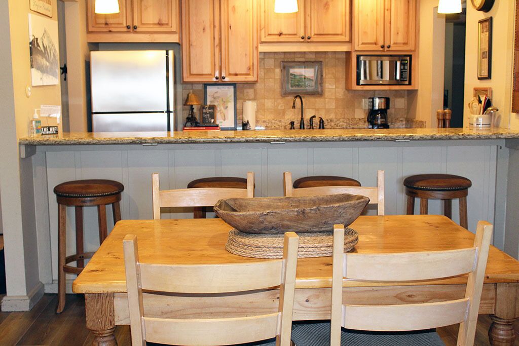 A kitchen with wooden cabinets, a granite countertop, a stainless steel refrigerator, and a dining table with four chairs.