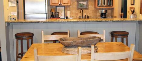 A kitchen with wooden cabinets, a granite countertop, a stainless steel refrigerator, and a dining table with four chairs.