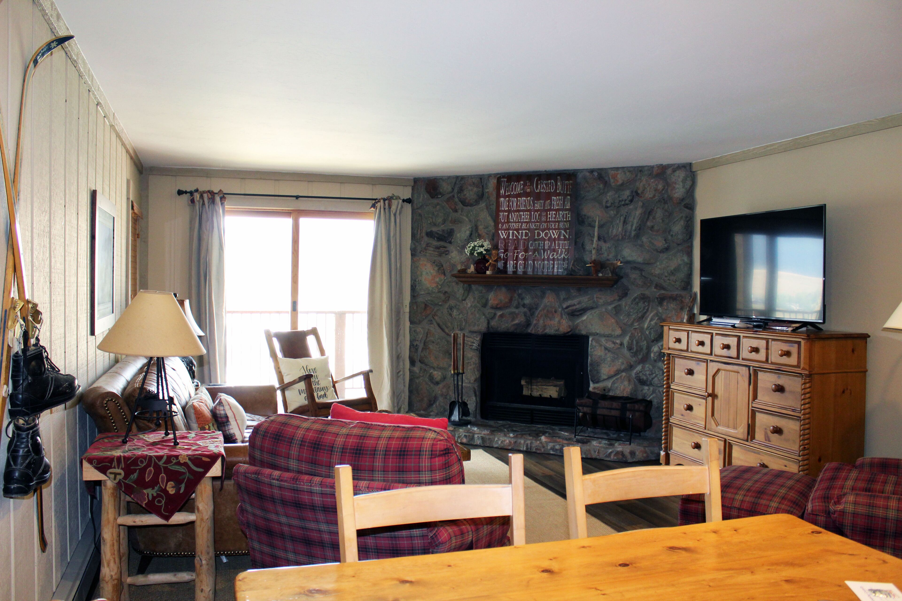 A cozy living room with a stone fireplace, plaid furniture, and a television.