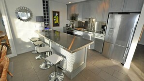 Eine moderne Küche mit Edelstahlgeräten, einer zentralen Kochinsel mit Barhocker und einem großen Kühlschrank.