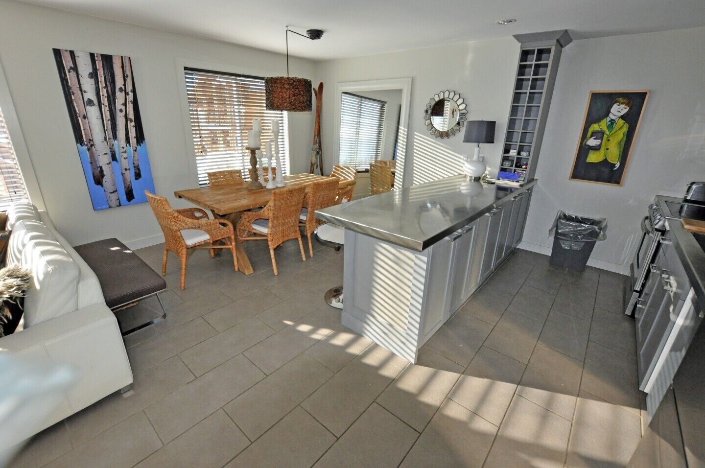Una cocina moderna con una isla central, comedor con sillas de mimbre y un sofá blanco.