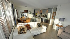 Ein modernes Wohnzimmer mit einem weißen Sofa, einem Essbereich und einer Küche im Hintergrund.