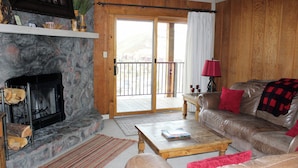 Una sala de estar acogedora con chimenea de piedra, sofá de cuero y un balcón con vistas.