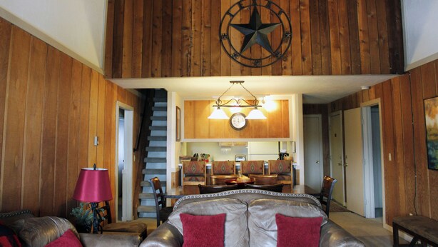 Amplia sala de estar con techo alto, decoración de estrella de madera, mesa de comedor con sillas y una escalera que conduce a otro nivel.