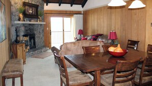 Un comedor acogedor con chimenea de piedra, paredes de madera y una gran mesa de comedor de madera con sillas.