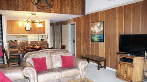 Una sala de estar con un sofá de cuero color beige, una mesa de centro de madera, un televisor y un mueble de madera.