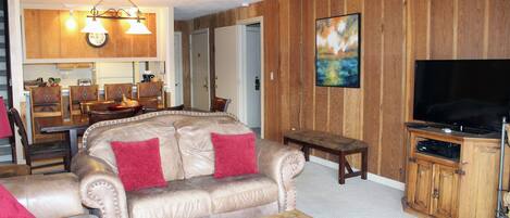 A living room with a beige leather sofa, a wooden coffee table, a television, and a wooden cabinet.