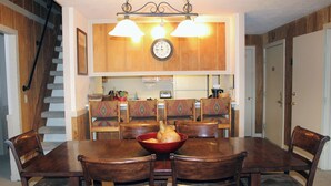 Un comedor con mesa y sillas de madera, un tazón rojo con comida y una cocina al fondo.