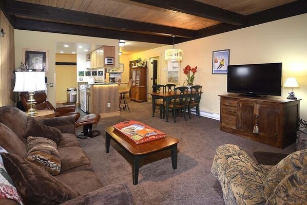 A living room with a sofa, coffee table, TV, and a dining area with chairs and a cabinet. - Steps Away from Adventure! Ski-In/Ski-Out Condo, Dog Friendly (Mt. Crested Butte)