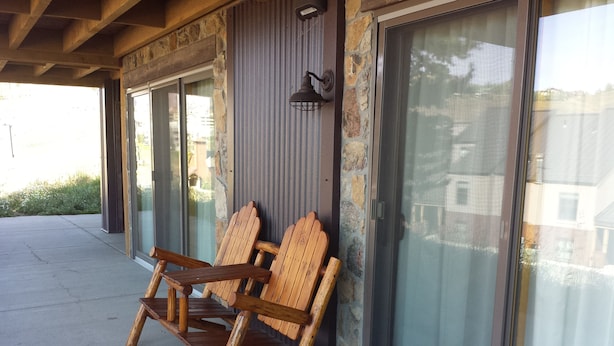 Två trästolar i Adirondack-stil står utomhus framför en byggnad med stora glasfönster och en mur av sten.